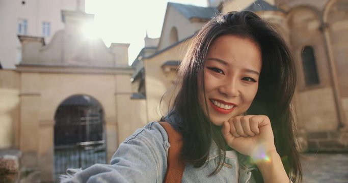 POV of the cheerful Asian charming woman in stylish look posing funny and nicely to the camera like taking selfie photo outside. Close up.