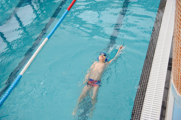 top view of a 7-year boy swimming backstroke in a swimming pool