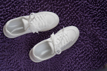 White clean ladies sneakers on a purple shaggy background. Fashionable summer women's and teenage shoes in white. For articles, blog