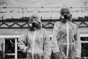 Fototapeta na wymiar Two scientists put on a respirator and a radiation protective suit. Stern look into the camera from the abandoned territory. Care about ecology in black and white photo mystical horror movie.