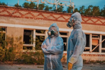 Two scientists put on a respirator and a radiation protective suit. Stern look into the camera from the abandoned territory. Care about ecology in bright saturated photos.