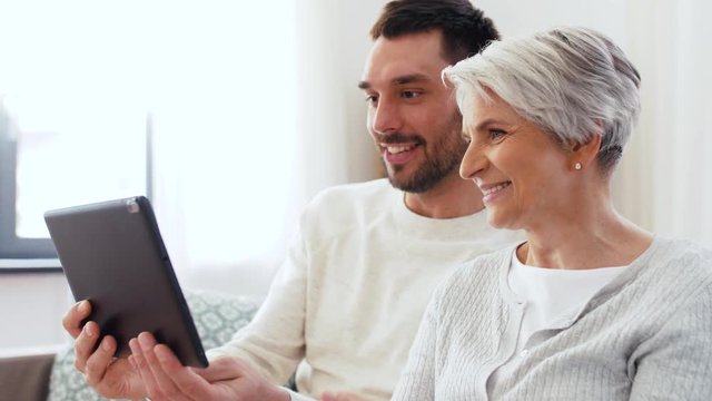 family, generation and people concept - happy smiling senior mother and adult son having video chat on tablet computer at home