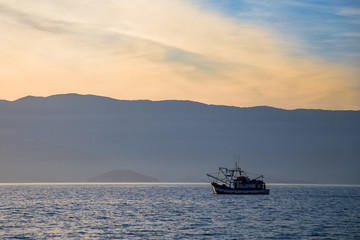 Solitary fishing boat navigating a generic sea with mountains skyline as background