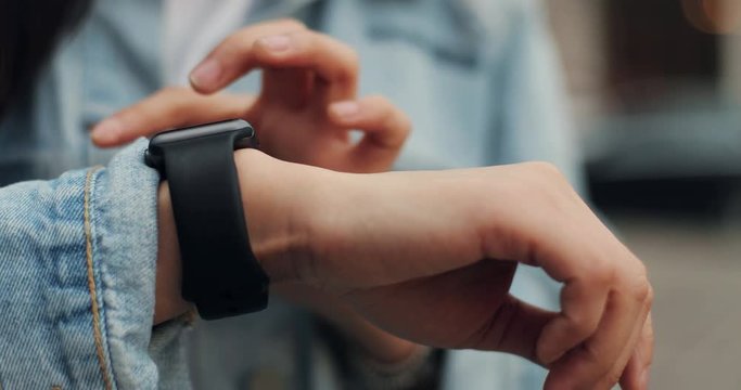 Close up of the Caucasian female hand typing and tapping on the smartwatch on her hand outside in the city center.