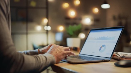 Close-up On the Hands of the Male Specialist Opening Laptop Computer and Starting Working, Screen Shows Various Data and Statistics. In the Background Evening in the Stylish Studio Office