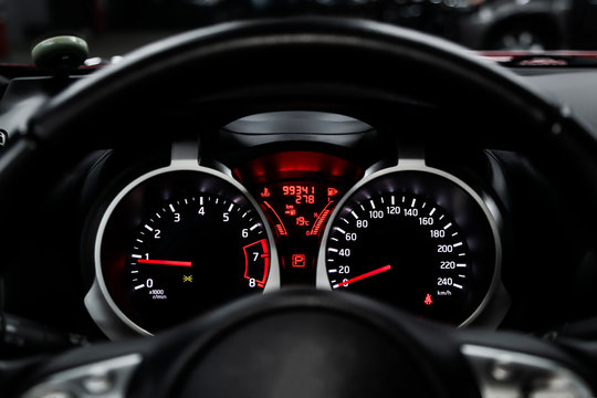 Car dashboard wuth red backlight: Odometer, speedometer, tachometer, fuel level, water temperature and more. Modern car interior: parts, buttons, knobs..