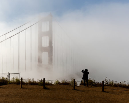 Photographing the Golden Gate Bridge in fog- silhouette of unidentifiable photographer  shooting the Golden Gate Bridge with a camera and a cell phone