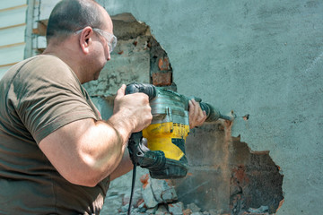 Dismantling walls and openings with an electric jackhammer. The worker in goggles performs repair...