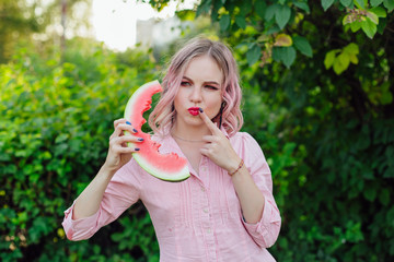 Beautiful emotional young woman with pink hair holding watermelon like telephone