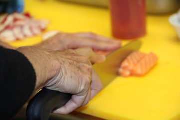 old woman chef cutting salmon fish on fillets with knife. Chef preparing food, Restaurant and cooking concept. drinks and food background.
