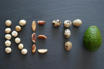 Keto diet.Low-carb foods. Brazil nuts, macadamia, quail eggs and avocados on a black slate background.	