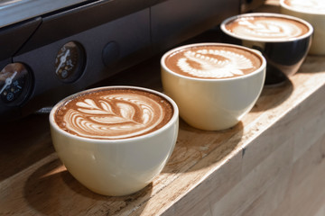 row of latte art coffee on wooden shelf