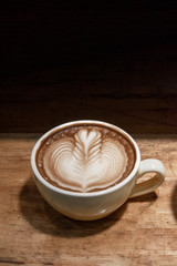 latte art coffee in coffee cup on wooden desk in black background