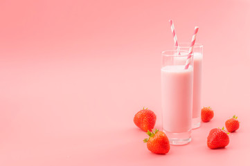 Summer refreshing desserts and calcium rich healthy drink concept theme with glasses of strawberry milk, striped straws and scattered strawberries isolated on pink background with copy space