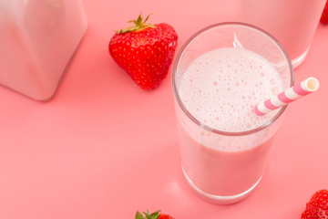 Summer refreshing desserts and calcium rich healthy drink concept theme with close up on glass of strawberry milk, striped straw and scattered strawberries isolated on pink background with copy space