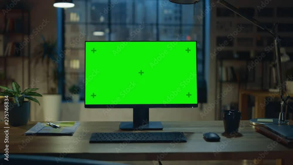 Poster Desktop Computer with Mock-up Green Screen Standing on the Wooden Desk in the Modern Creative Office. In the Background Warm Evening Lighting and Open Space Studio with City Window View. Zoom Out Shot