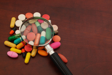 Colorful drugs and magnifying glass on wooden table with room for text, medical drugs review