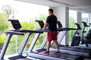 chubby man walking on running track, warming up on gym treadmill. back view