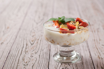 Bowl of yogurt and oatmeal decorated with strawberries on a rustic table.