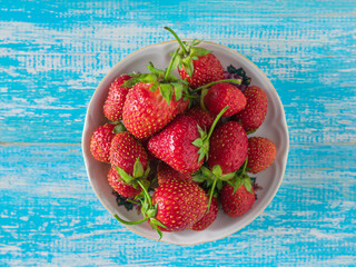 Bowl with ripe strawberries on a blue wooden background. Harvest of fresh berries. Flat lay.