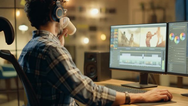Evening in Creative Office: Professional Videographer / Audio Engineer Wearing Headphones Works on Desktop Computer, Screen Shows: Footage Montage, Using Video Editing Software, Syncing Audio Track