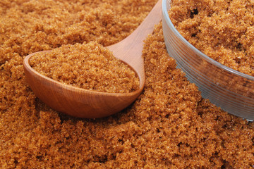 Dark brown sugar in wooden spoon, glass bowl and on table