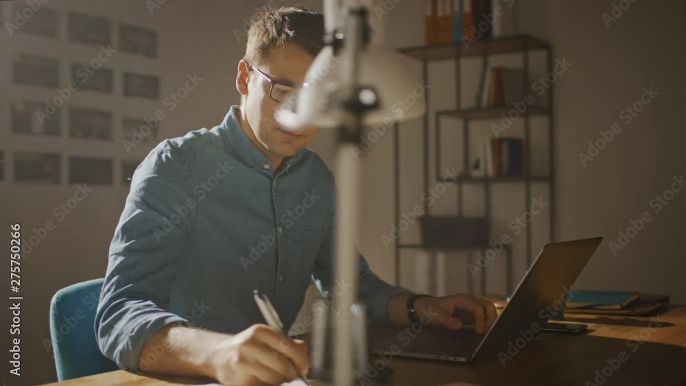 Poster Professional Creative Man Sitting at His Desk in Home Office Studio Working on a Laptop. Man working with Data and Analyzing Statistics. Camera Moving Around. 360 Degree Tracking Arc Shot Movement