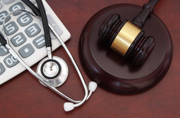 Gavel, calculator and stethoscope on wooden table