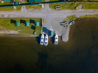 Aerial view of the road in the village with gazebos and the road in the Altai Mountains on the shore of Lake Teletskoye with three boat moored near the shore. Leisure and outdoor travel without people