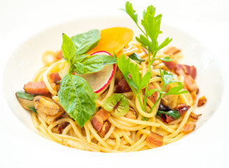 Close up picture of spaghetti bacon fried with dry chilli in white ceramic placte.