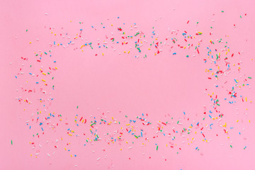 trendy frame of colorful sprinkles over pink background, decoration for cake and bakery
