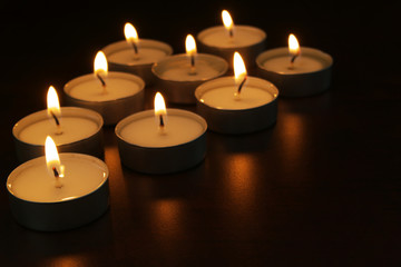 Fototapeta na wymiar Burning candles on table in darkness. Romance, celebration and memorial symbol.