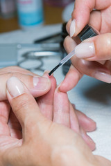 Obraz na płótnie Canvas woman hand on manicure treatment with cuticle knife in beauty salon. applying a brush on acrylic nails in the salon. vertical photo
