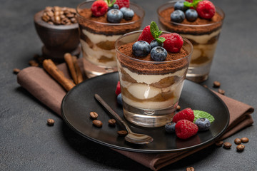 Classic tiramisu dessert with blueberries and raspberries in a glass on dark concrete background