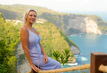 young happy and beautiful blond woman relaxed at tropical beach cliff viewpoint enjoying Summer holidays getaway carefree at paradise island in tourist travel