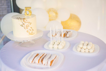 Candy bar and white cake decorated golden confectionery sprinkles decorated candle number five on white background
