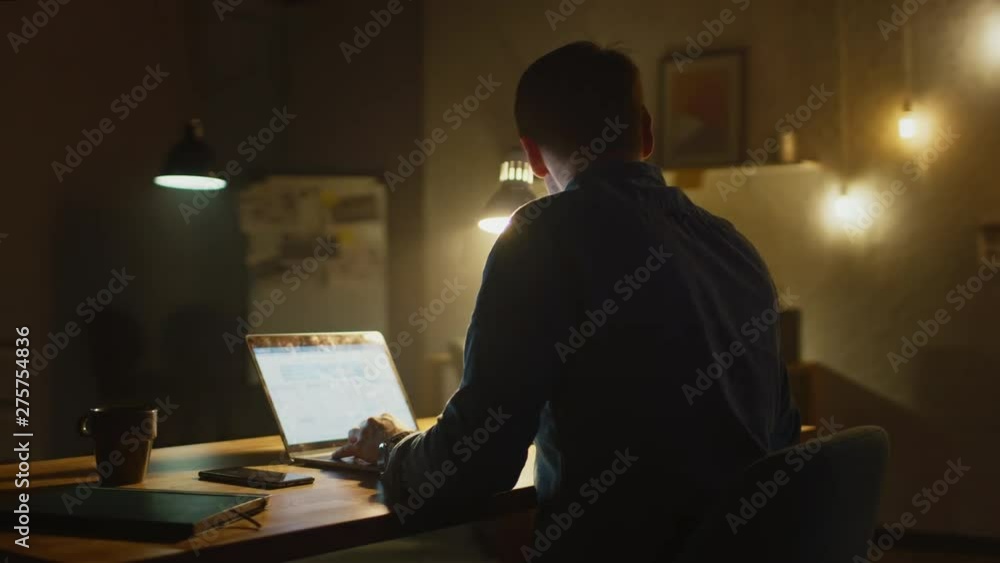 Aufkleber Professional Creative Man Sitting at His Desk in Office Studio Working on Laptop in the Evening. Man working with Data and Analyzing Statistics, Using Smartphone. 360 Degree Tracking Arc Shot Movement