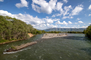 River flowing between green hills with snow-capped mountain peaks on the horizon against a cloudy sky