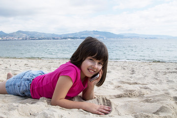 Fototapeta na wymiar girl lying on the sand with the mobile phone