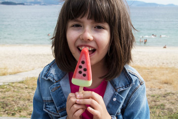 little girl eating a watermelon ice cream with beach background