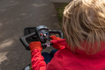 An over the shoulder shot of an elderly lady in a red coat enjoying the freedom of an electric mobility scooter, three quarters of the head showing