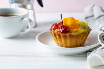 Homemade fruit tart with orange kiwi and cherry on white plate