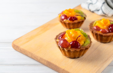 Mini mixed fruit tarts with orange cherry and kiwi on wooden plate