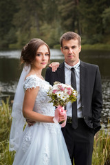 Portrait of wedding couple. Bride and groom embracing in the park against the background of the lake and forest. Sunny autumn day