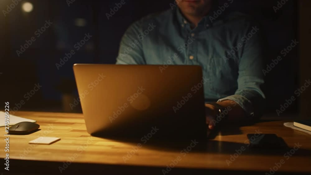 Poster  Anonymous Man Sitting at His Desk in Office Studio Working on a Laptop in the Evening. Man working with Data, Analyzing Statistics. Energetic Fast Paced Movement 360 Degree Tracking Arc Shot Movement