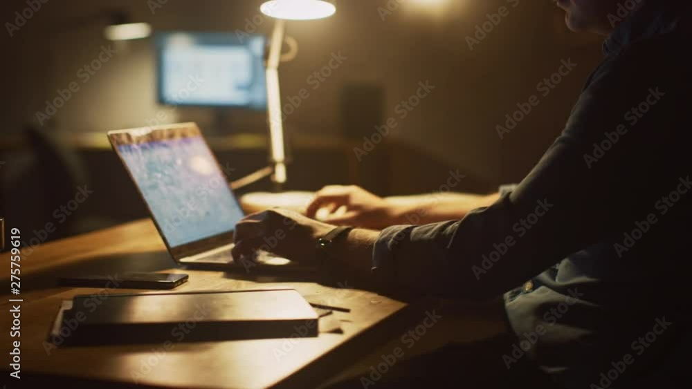Aufkleber  Anonymous Man Sitting at His Desk in Office Studio Working on a Laptop in the Evening. Man working with Data, Analyzing Statistics. 360 Degree Tracking Arc Shot Movement