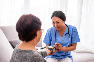 Happy senior woman having her blood pressure measured in a nursing home by her caregiver. Happy...