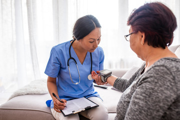 Fototapeta premium Asian nurse doing blood pressure monitoring for senior woman at home. Close up photo of blood pressure measurement. Nurse measuring blood pressure of senior woman at home. Smiling to each other.