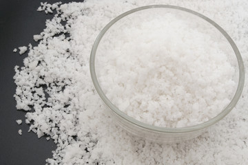 Glass bowl with sea salt on black background