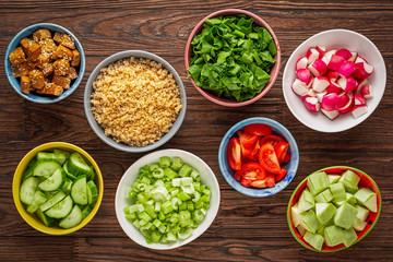 Ingredients of healthy nutrition in colorful bowls on a wooden table. Quinoa, raw vegetables and fried tofu